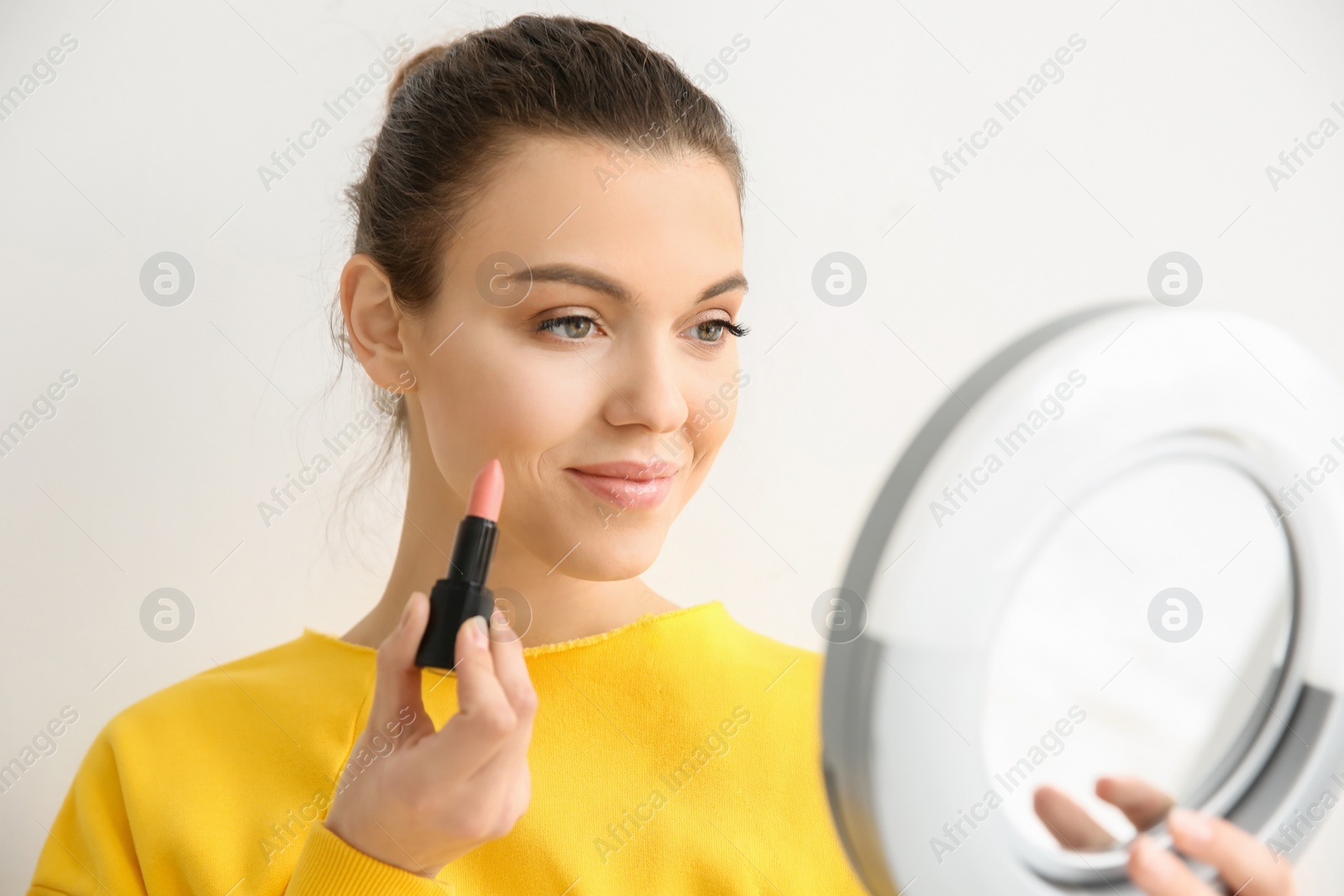 Young woman applying lipstick on light background. Professional makeup products Photo of Young woman applying lipstick on light background. Professional makeup products