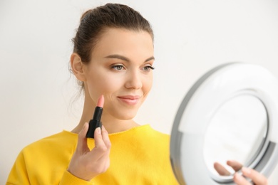 Young woman applying lipstick on light background. Professional makeup products Photo of Young woman applying lipstick on light background. Professional makeup products