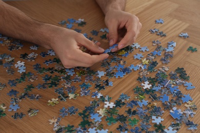 Man playing with puzzles at wooden table, closeup Photo of Man playing with puzzles at wooden table, closeup