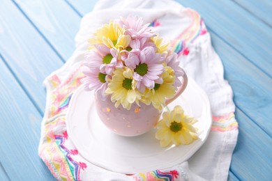 Bouquet of beautiful flowers in cup on light blue wooden table Photo of Bouquet of beautiful flowers in cup on light blue wooden table