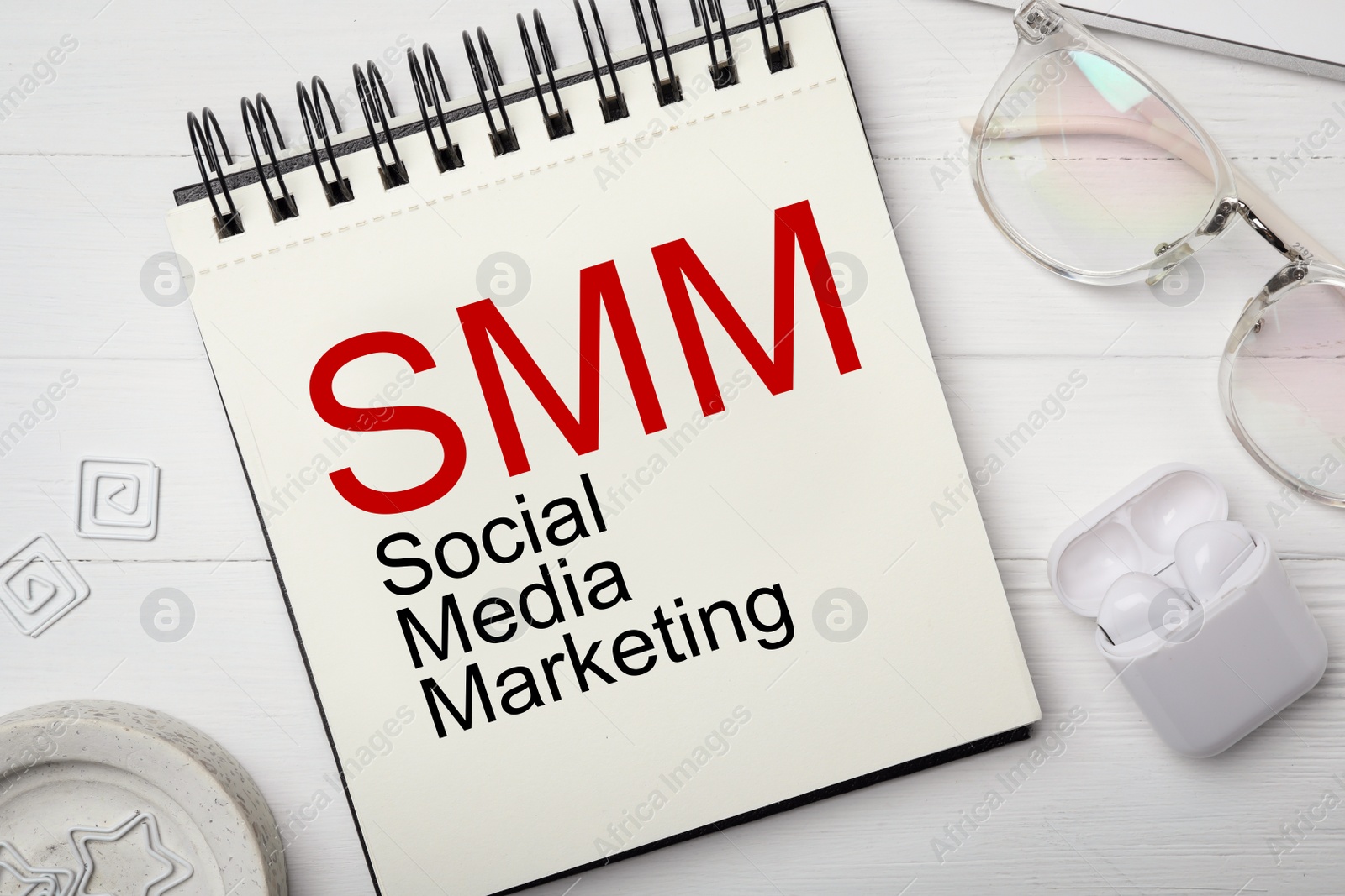 Notebook with text SMM (Social media marketing), eyeglasses and earphones on white wooden table, flat lay Image of Notebook with text SMM (Social media marketing), eyeglasses and earphones on white wooden table, flat lay
