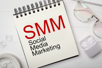 Notebook with text SMM (Social media marketing), eyeglasses and earphones on white wooden table, flat lay Image of Notebook with text SMM (Social media marketing), eyeglasses and earphones on white wooden table, flat lay