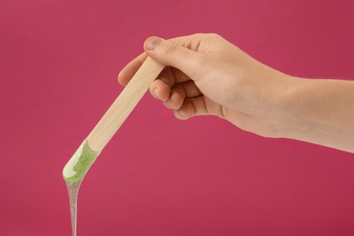 Woman holding spatula with hot depilatory wax on fuchsia background, closeup Photo of Woman holding spatula with hot depilatory wax on fuchsia background, closeup