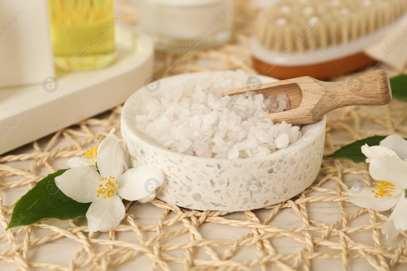 Sea salt in bowl and beautiful jasmine flowers on white table Photo of Sea salt in bowl and beautiful jasmine flowers on white table