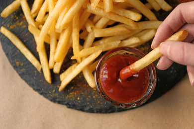 Woman dipping French fries into red sauce in cafe, closeup Photo of Woman dipping French fries into red sauce in cafe, closeup