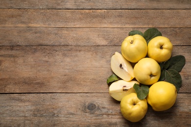 Photo of Fresh ripe organic quinces with leaves on wooden table, flat lay. Space for text