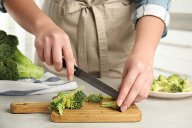 Woman cutting raw broccoli at light grey marble table, closeup Photo of Woman cutting raw broccoli at light grey marble table, closeup
