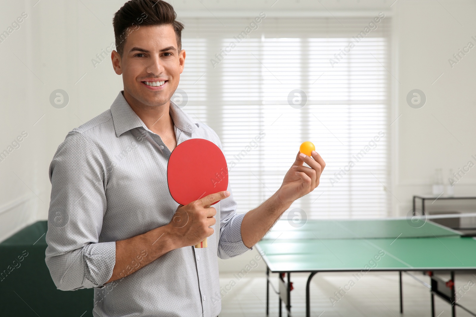Businessman with tennis racket and ball near ping pong table in office. Space for text Photo of Businessman with tennis racket and ball near ping pong table in office. Space for text