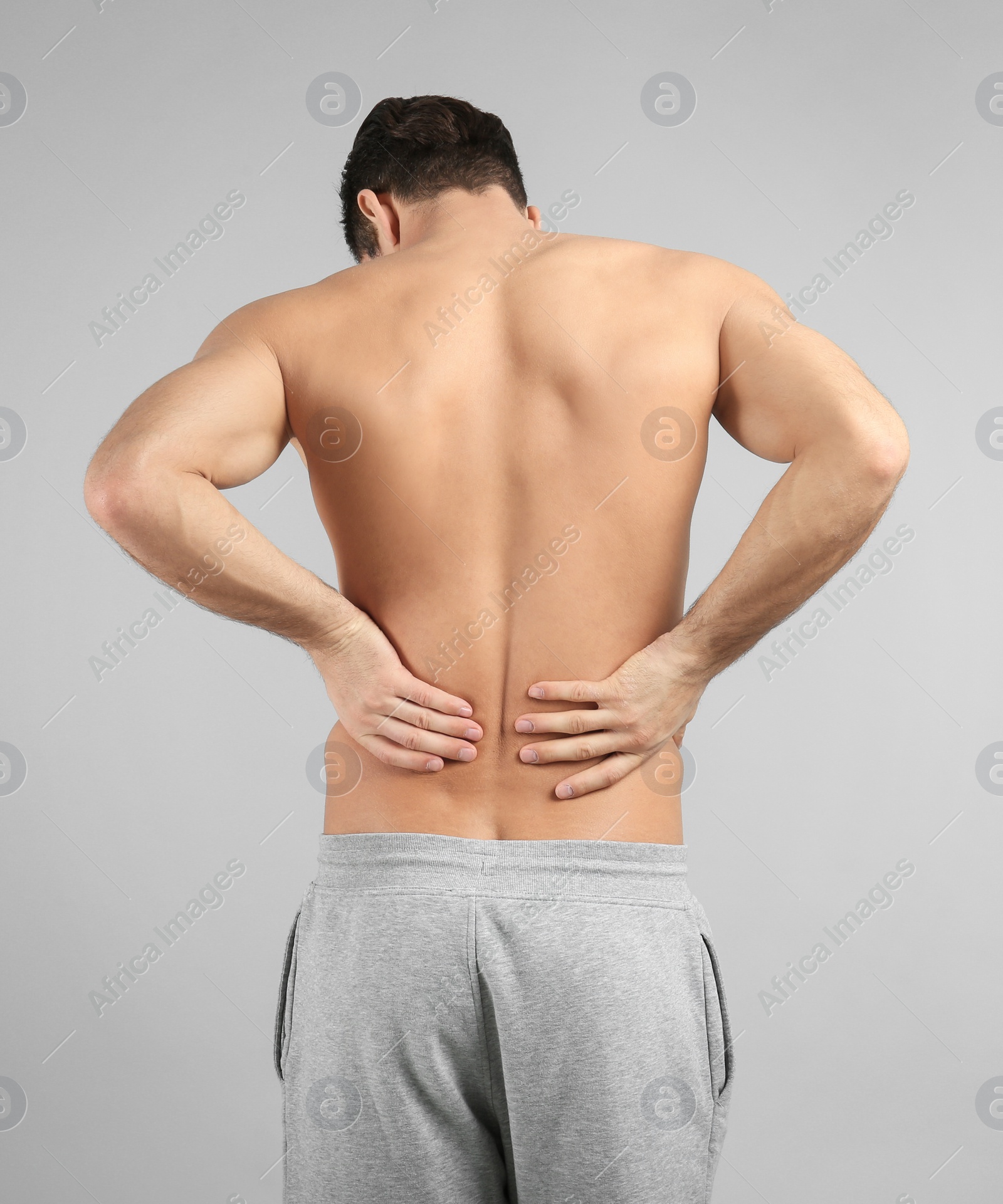 Young man suffering from back pain on grey background Photo of Young man suffering from back pain on grey background