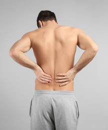 Young man suffering from back pain on grey background Photo of Young man suffering from back pain on grey background
