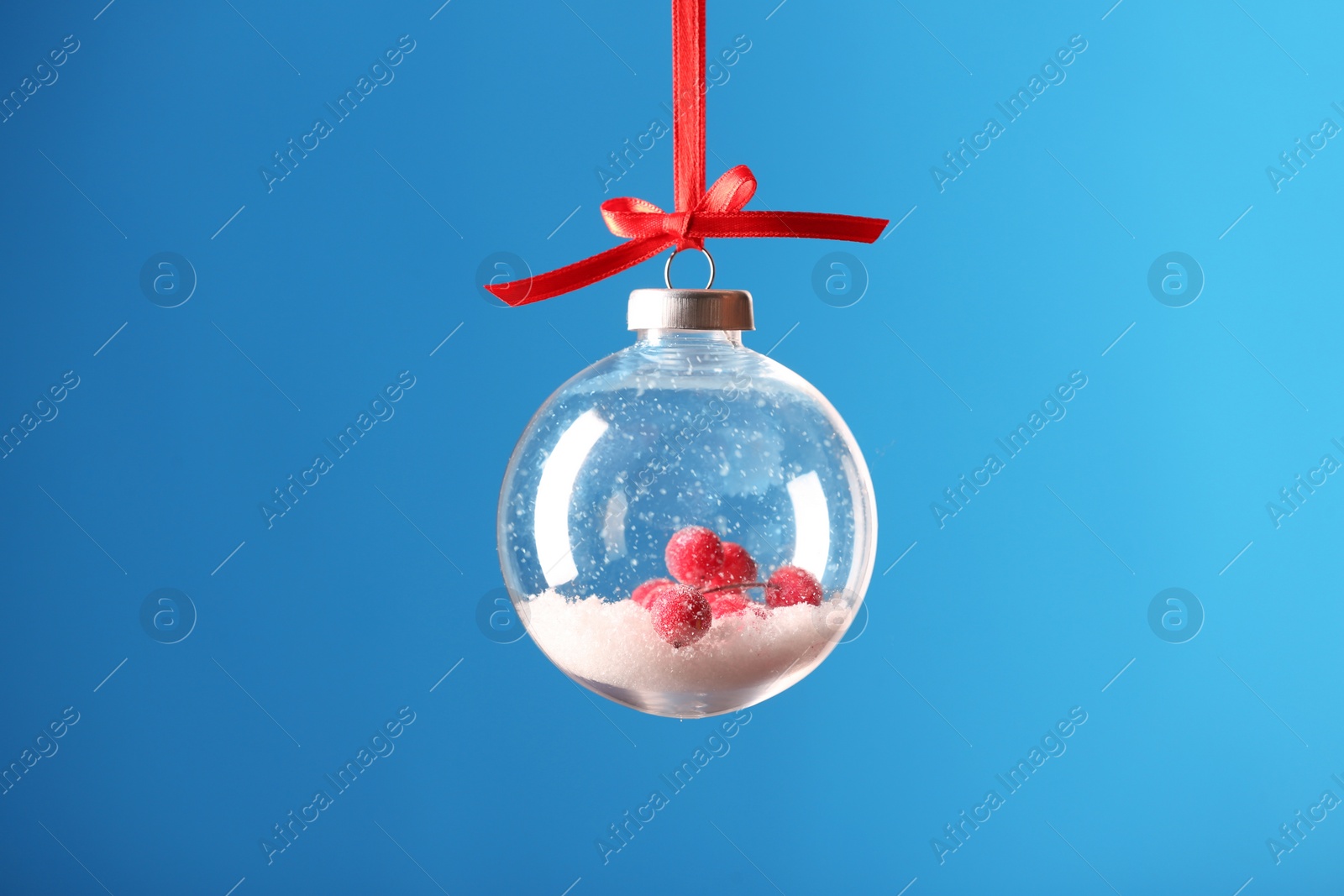 Decorative snow globe hanging on light blue background Photo of Decorative snow globe hanging on light blue background
