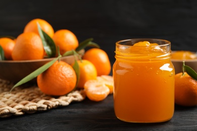 Tasty tangerine jam in glass jar on dark wooden table. Space for text Photo of Tasty tangerine jam in glass jar on dark wooden table. Space for text