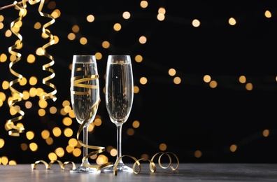 Glasses of champagne and serpentine streamers against black background with blurred lights. Space for text Photo of Glasses of champagne and serpentine streamers against black background with blurred lights. Space for text