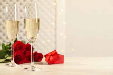 Beautiful engagement ring with gemstone in glass of sparkling wine and roses on white wooden table. Space for text Photo of Beautiful engagement ring with gemstone in glass of sparkling wine and roses on white wooden table. Space for text