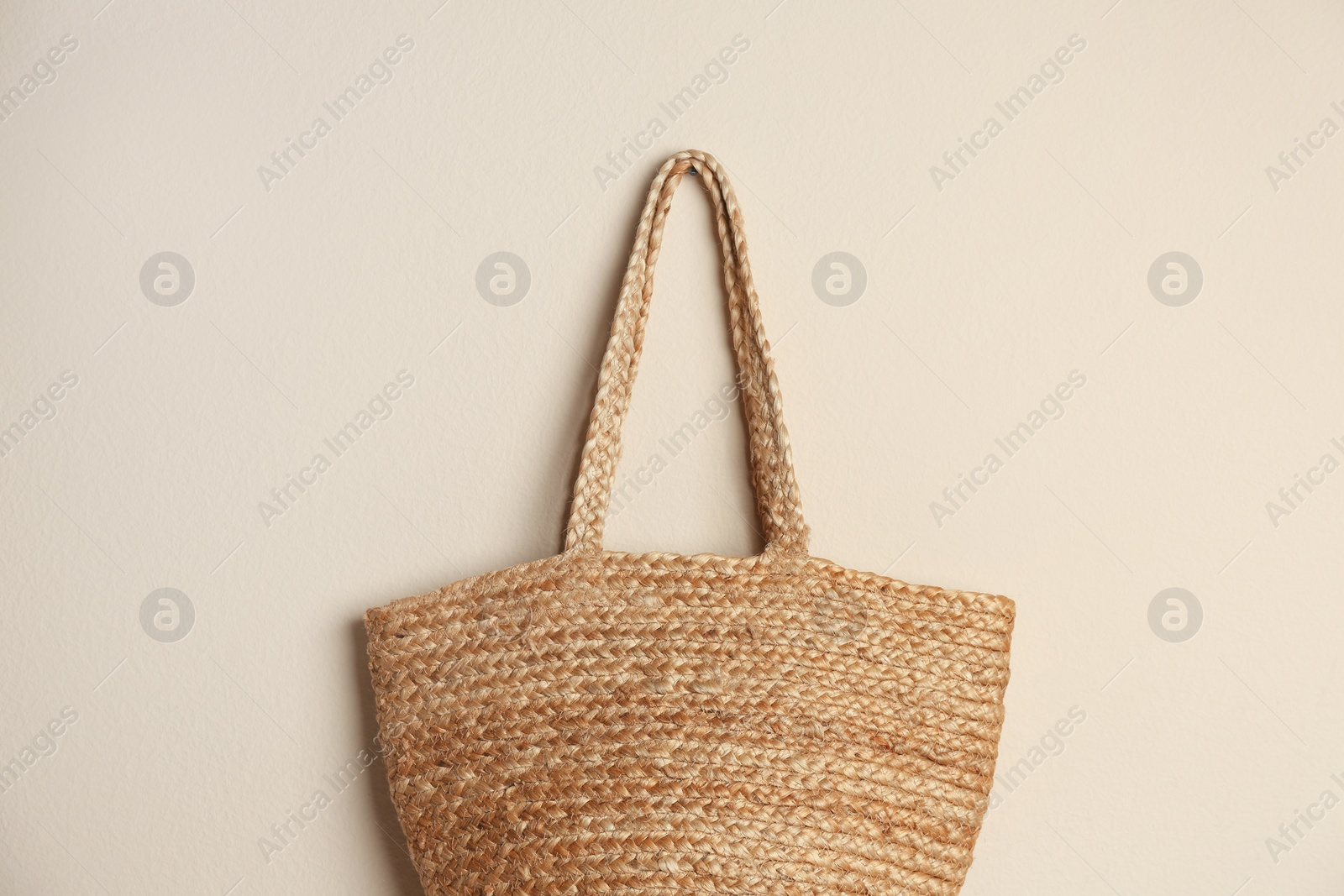 Elegant woman's straw bag hanging on beige background Photo of Elegant woman's straw bag hanging on beige background