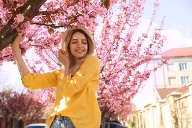 Happy stylish young woman near blossoming sakura tree outdoors. Spring look Photo of Happy stylish young woman near blossoming sakura tree outdoors. Spring look