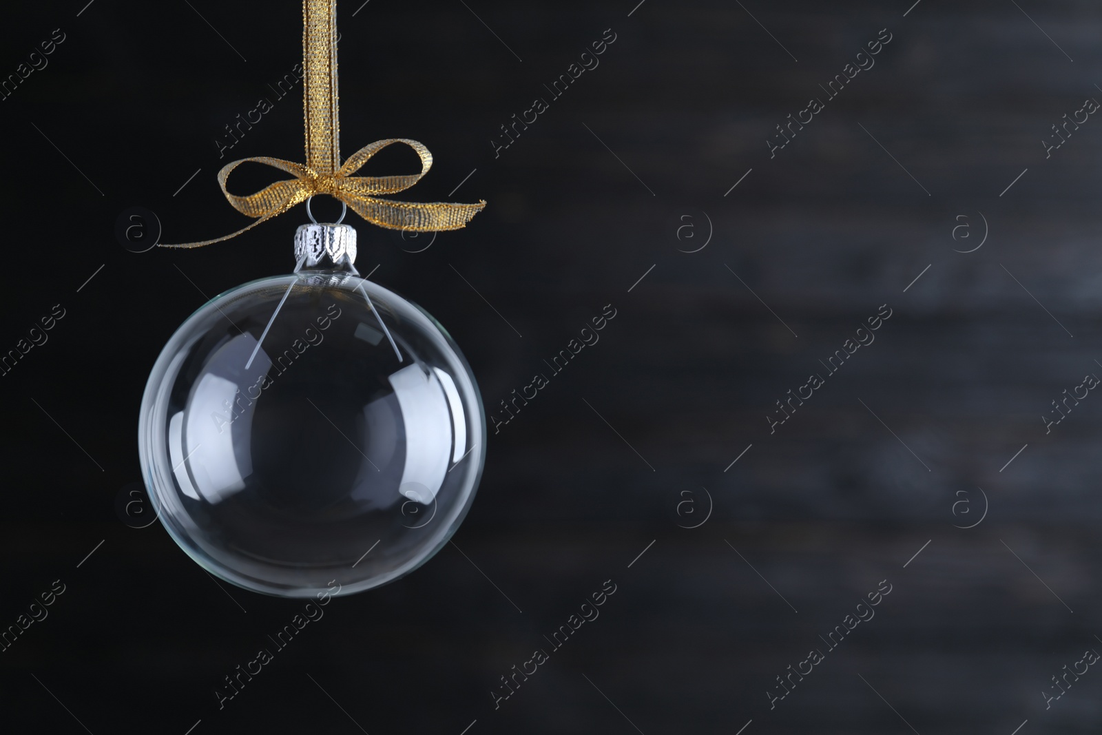 Transparent glass Christmas ball with golden ribbon and bow on dark background. Space for text Photo of Transparent glass Christmas ball with golden ribbon and bow on dark background. Space for text