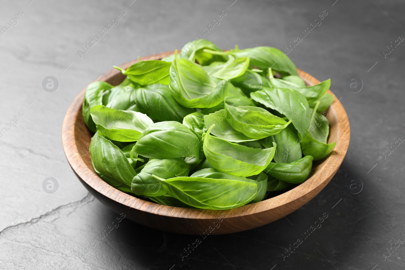 Fresh basil leaves in bowl on grey table Photo of Fresh basil leaves in bowl on grey table