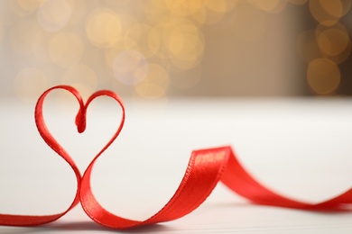 Heart made of red ribbon on table against blurred festive lights, space for text. Valentine's day celebration Photo of Heart made of red ribbon on table against blurred festive lights, space for text. Valentine's day celebration