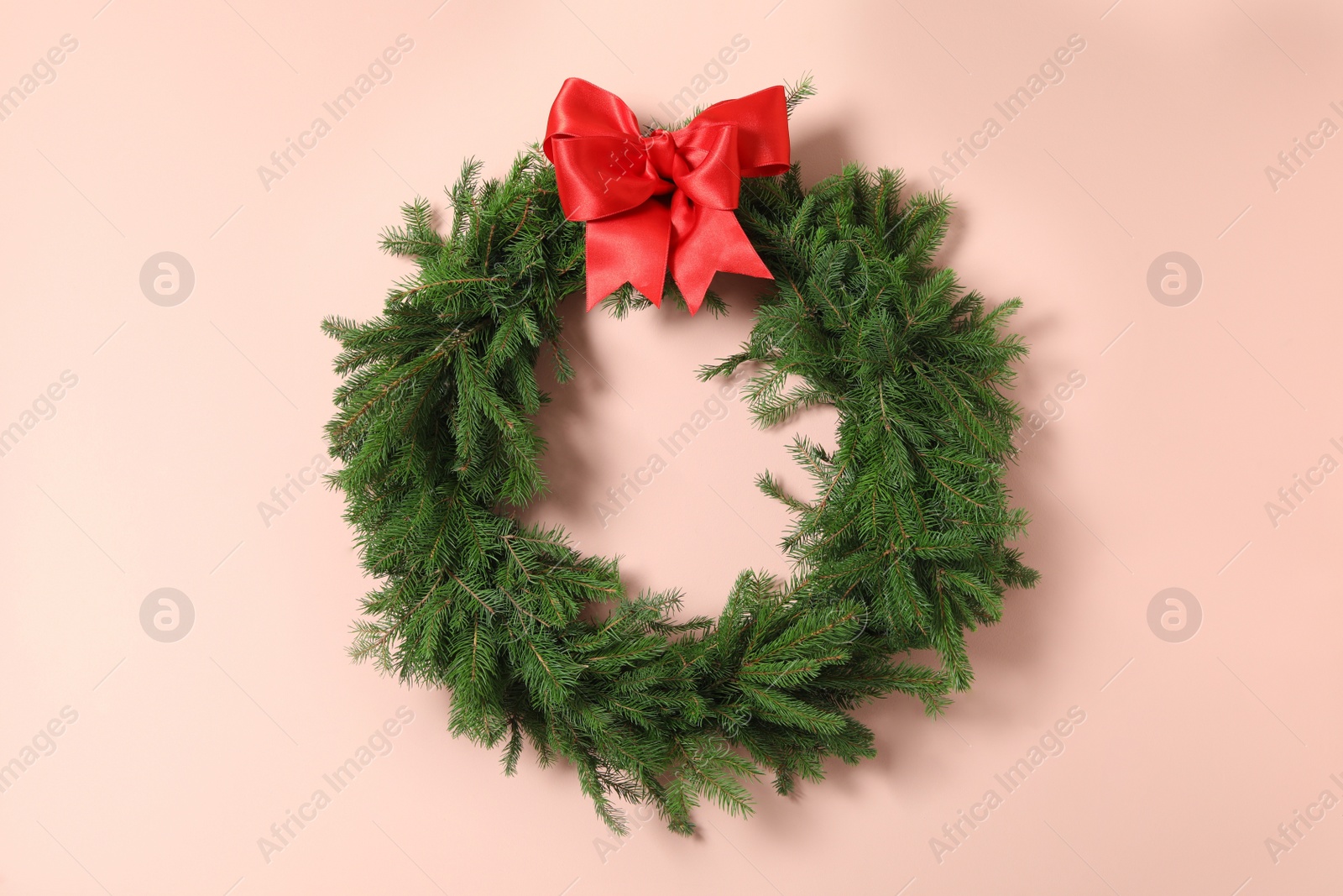 Christmas wreath made of fir branches with red bow on pink background Photo of Christmas wreath made of fir branches with red bow on pink background