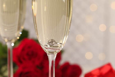 Beautiful engagement ring with gemstone in glass of sparkling wine, closeup Photo of Beautiful engagement ring with gemstone in glass of sparkling wine, closeup