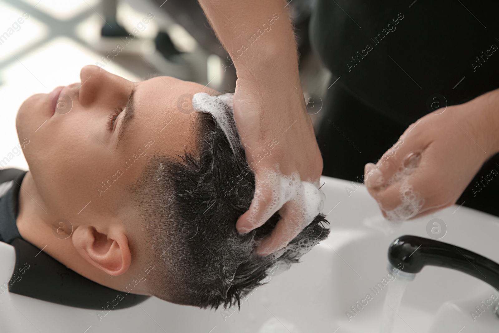 Photo of Professional barber washing client's hair at sink in salon, closeup