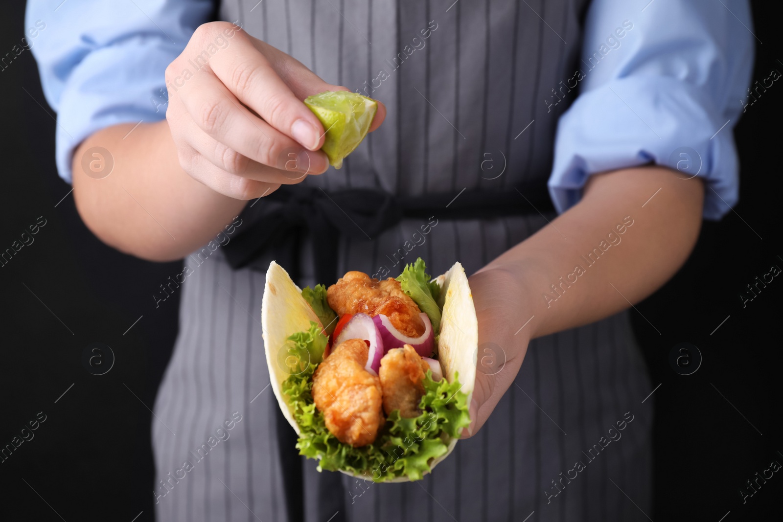 Woman squeezing lime on fish taco against dark background, closeup Photo of Woman squeezing lime on fish taco against dark background, closeup