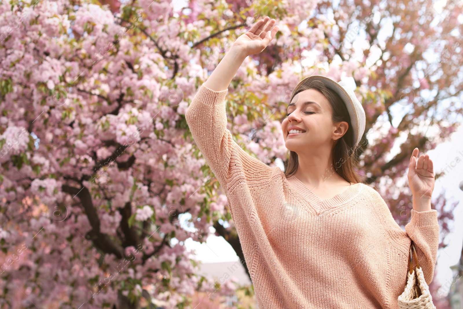 Happy stylish young woman near blossoming sakura tree outdoors. Spring look Photo of Happy stylish young woman near blossoming sakura tree outdoors. Spring look