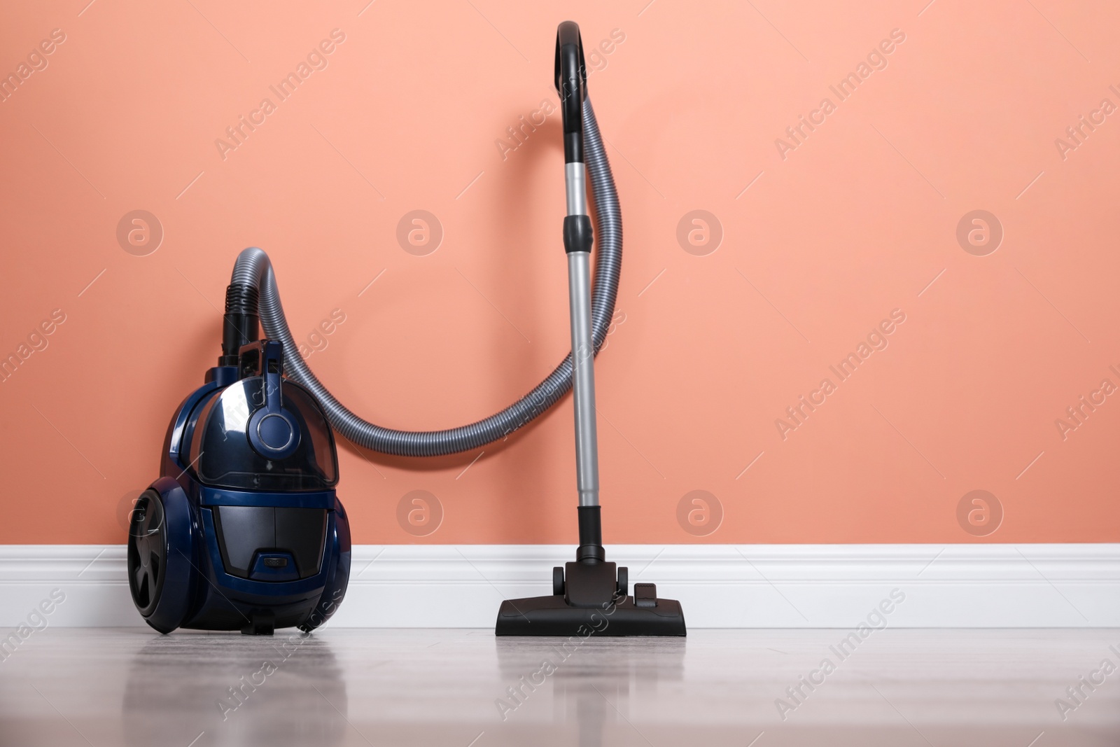 Modern vacuum cleaner on floor near orange wall indoors. Space for text Photo of Modern vacuum cleaner on floor near orange wall indoors. Space for text