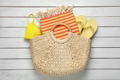 Beach bag with towel, flip flops and swimsuit on white wooden background, top view Photo of Beach bag with towel, flip flops and swimsuit on white wooden background, top view