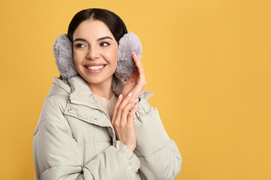 Beautiful young woman wearing earmuffs on yellow background. Space for text Photo of Beautiful young woman wearing earmuffs on yellow background. Space for text