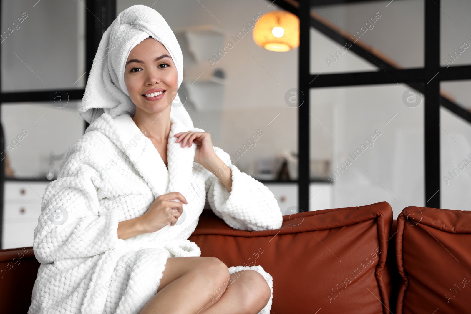 Young woman with towel wearing bathrobe in room Photo of Young woman with towel wearing bathrobe in room
