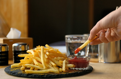 Woman dipping French fries into red sauce in cafe, closeup Photo of Woman dipping French fries into red sauce in cafe, closeup