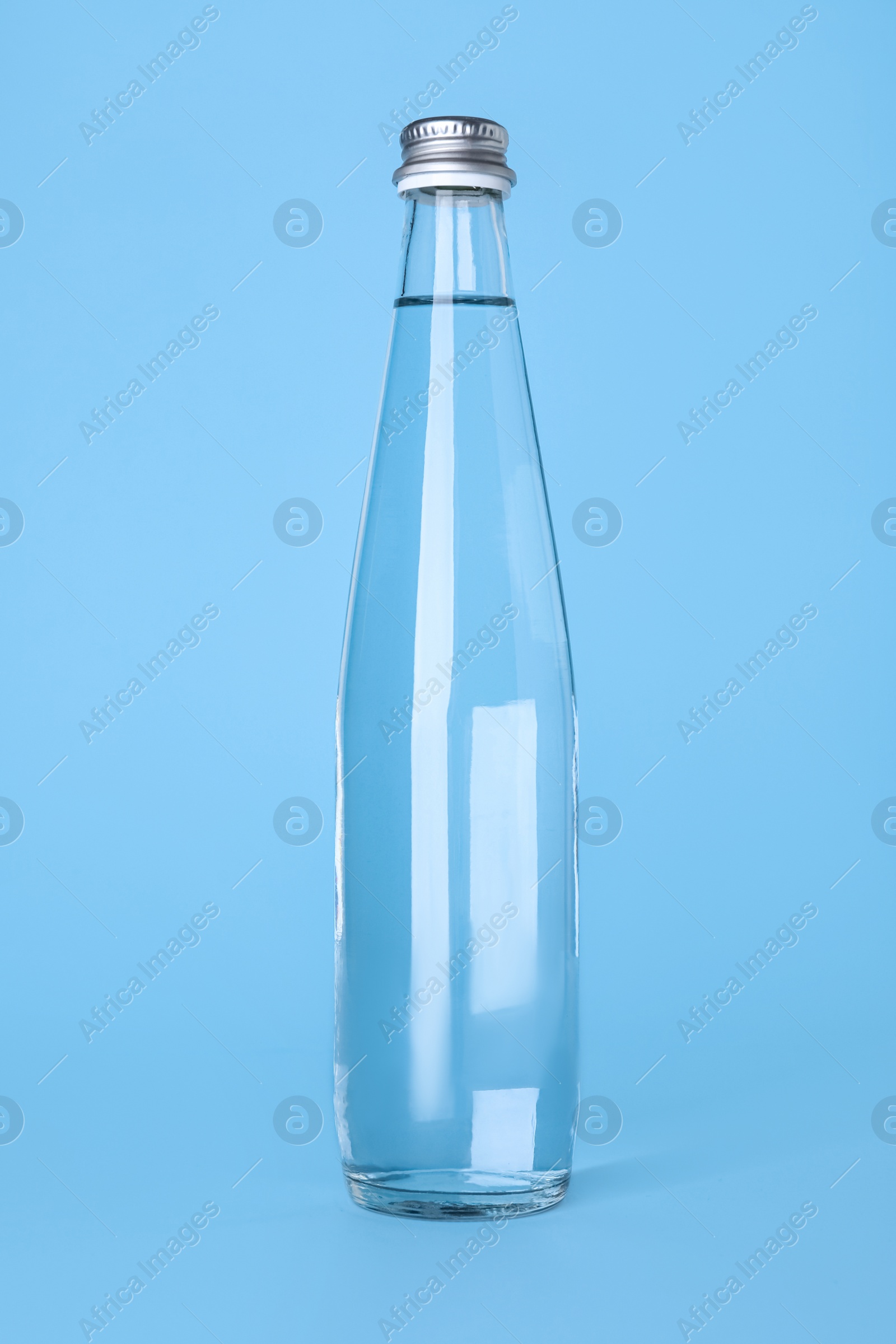 Glass bottle with water on light blue background Photo of Glass bottle with water on light blue background