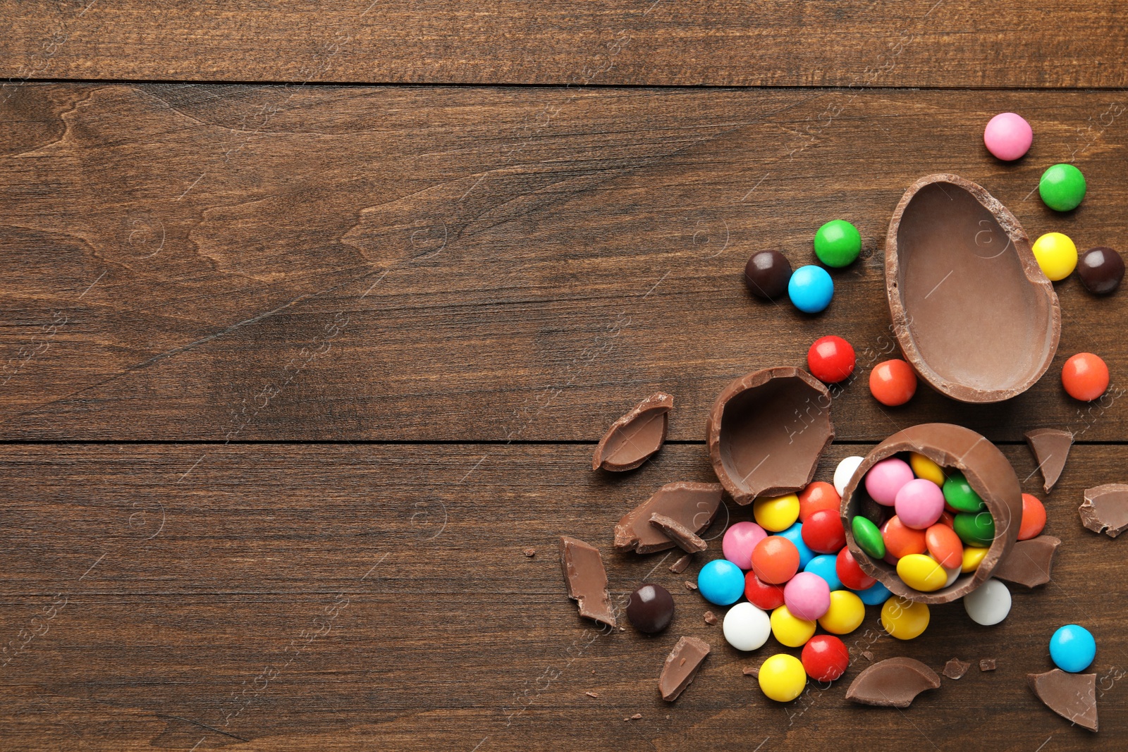 Photo of Broken chocolate eggs and colorful candies on wooden table, flat lay. Space for text