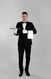 Handsome butler with tray on light grey background Photo of Handsome butler with tray on light grey background