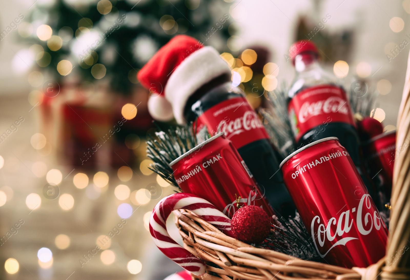 MYKOLAIV, UKRAINE - January 01, 2021: Basket with Coca-Cola drinks against blurred Christmas lights, closeup Photo of MYKOLAIV, UKRAINE - January 01, 2021: Basket with Coca-Cola drinks against blurred Christmas lights, closeup