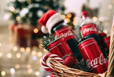 MYKOLAIV, UKRAINE - January 01, 2021: Basket with Coca-Cola drinks against blurred Christmas lights, closeup Photo of MYKOLAIV, UKRAINE - January 01, 2021: Basket with Coca-Cola drinks against blurred Christmas lights, closeup