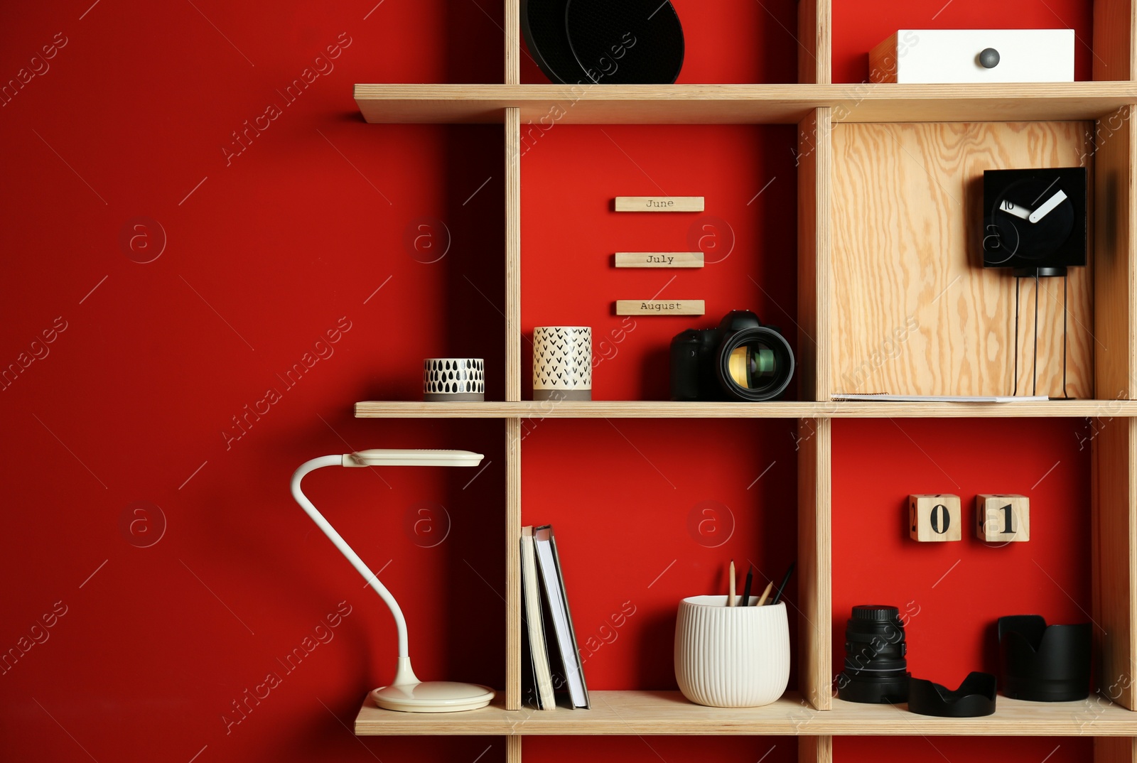 Stylish wooden shelves with photography equipment and decorative elements on red wall Photo of Stylish wooden shelves with photography equipment and decorative elements on red wall