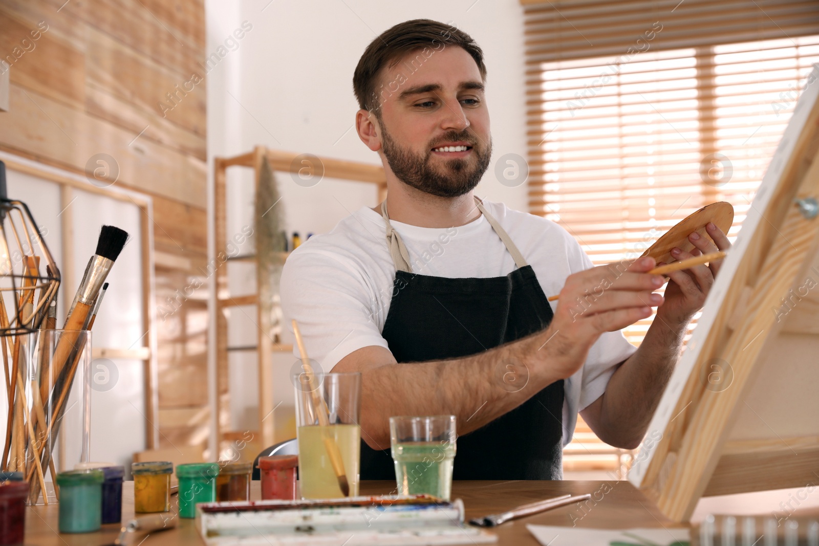 Young man painting on easel with brush in artist studio Photo of Young man painting on easel with brush in artist studio