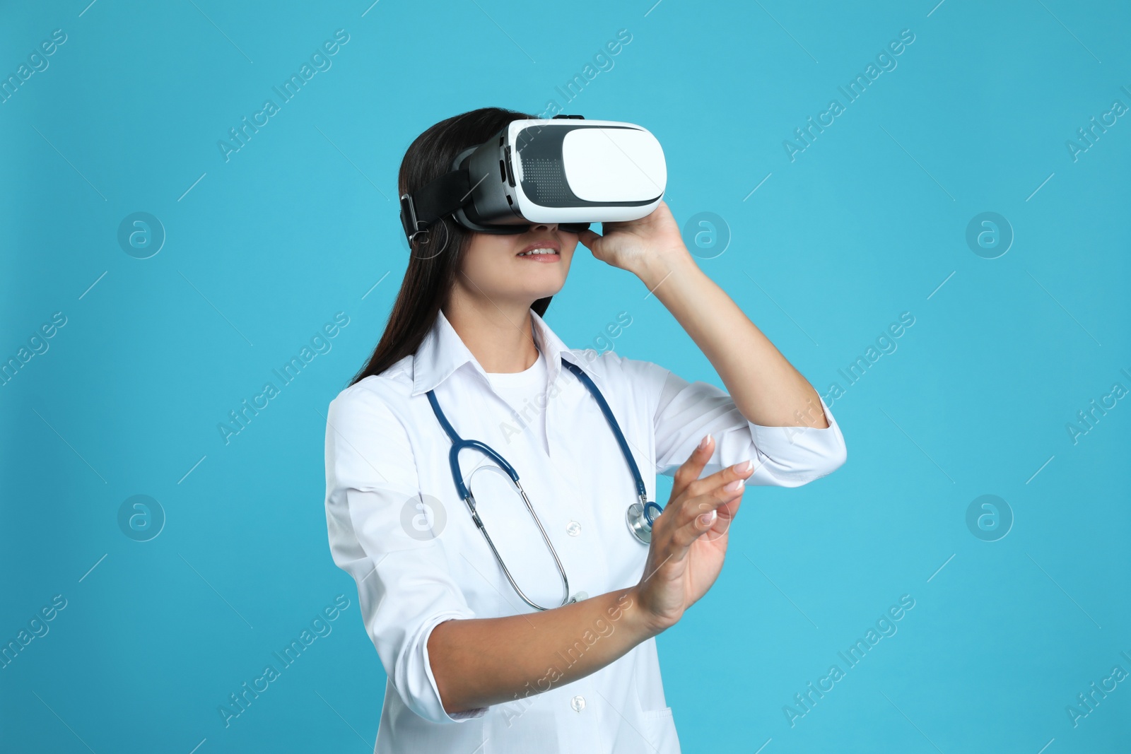 Female doctor using virtual reality headset on light blue background Photo of Female doctor using virtual reality headset on light blue background