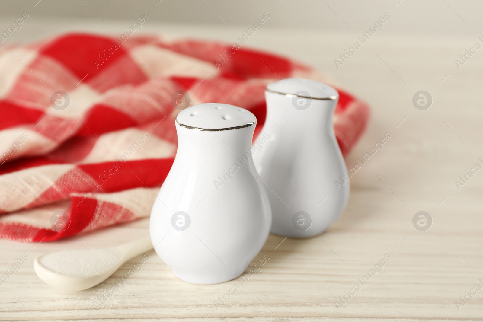 Ceramic salt and pepper shakers, spoon with napkin on white wooden table, closeup Photo of Ceramic salt and pepper shakers, spoon with napkin on white wooden table, closeup