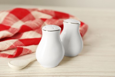 Ceramic salt and pepper shakers, spoon with napkin on white wooden table, closeup Photo of Ceramic salt and pepper shakers, spoon with napkin on white wooden table, closeup