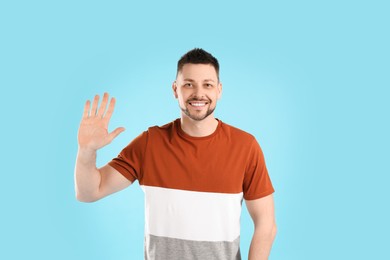 Cheerful man waving to say hello on light blue background Photo of Cheerful man waving to say hello on light blue background