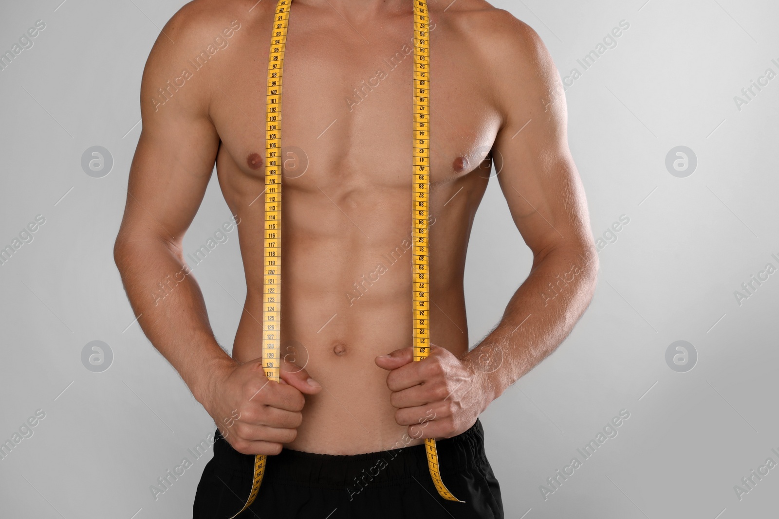 Shirtless man with slim body and measuring tape on grey background, closeup Photo of Shirtless man with slim body and measuring tape on grey background, closeup