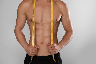 Shirtless man with slim body and measuring tape on grey background, closeup Photo of Shirtless man with slim body and measuring tape on grey background, closeup