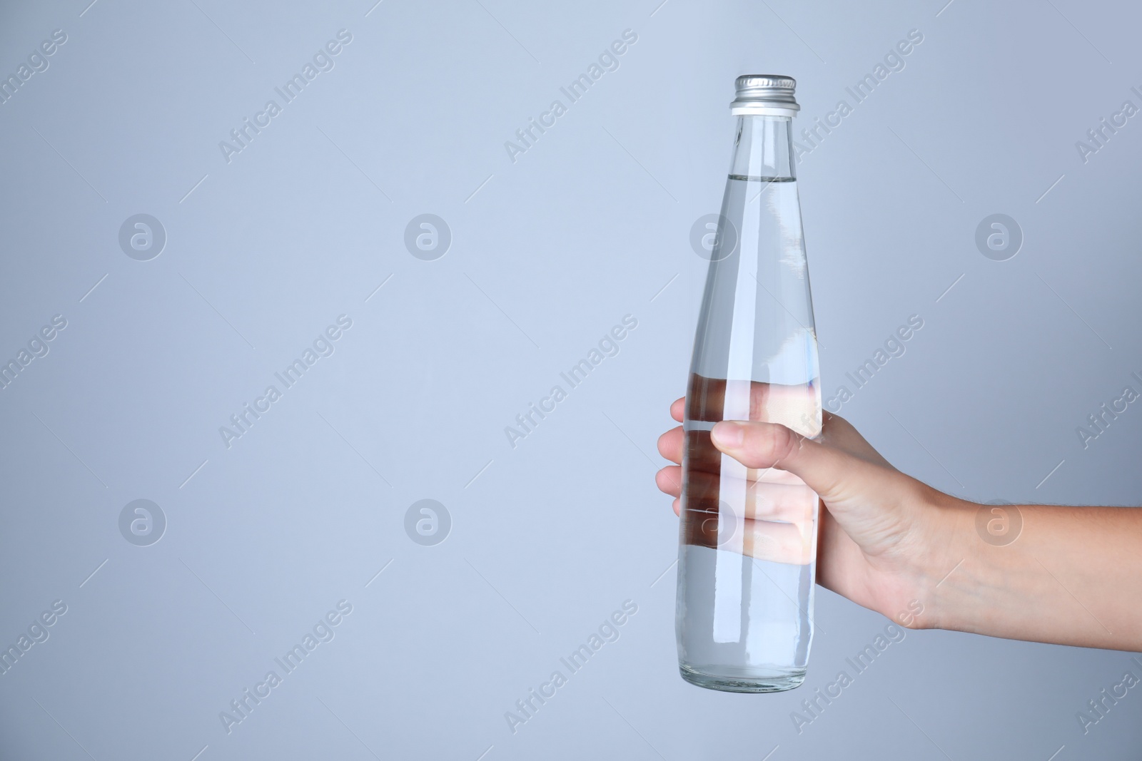 Woman holding glass bottle with water on white background, closeup. Space for text Photo of Woman holding glass bottle with water on white background, closeup. Space for text