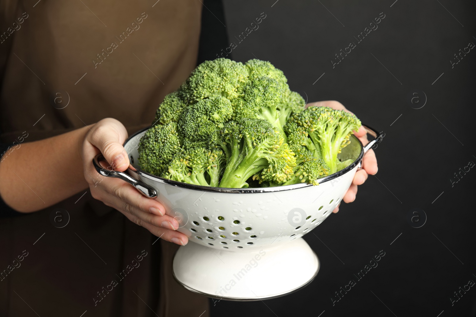 Woman holding colander with fresh green broccoli on black background, closeup Photo of Woman holding colander with fresh green broccoli on black background, closeup