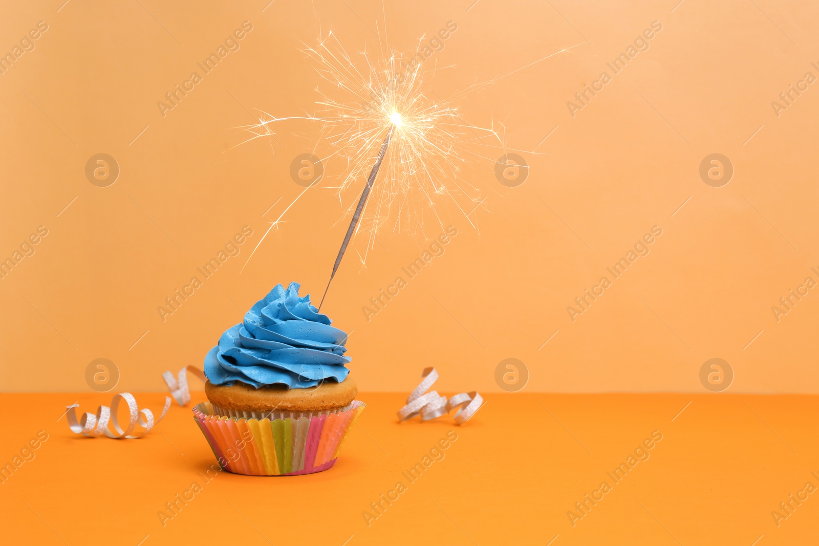 Birthday cupcake with sparkler on color background Photo of Birthday cupcake with sparkler on color background