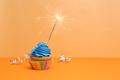 Birthday cupcake with sparkler on color background Photo of Birthday cupcake with sparkler on color background